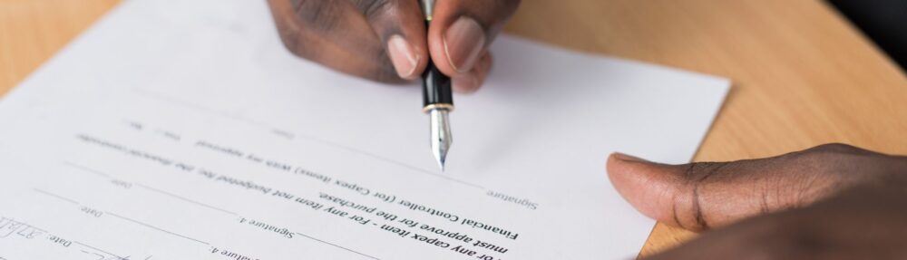 A hand signing a contract with a fountain pen