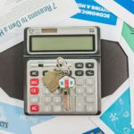 Calculator with keys and real estate documents symbolizes home buying finances.