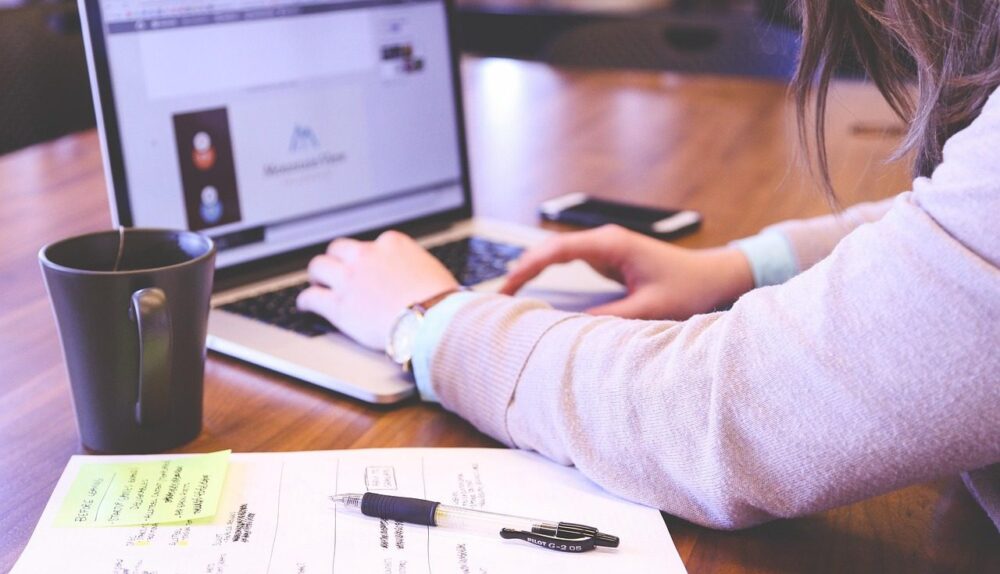 Business owner typing on a laptop beside notes and a coffee mug