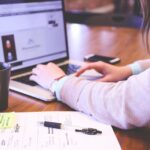 Business owner typing on a laptop beside notes and a coffee mug