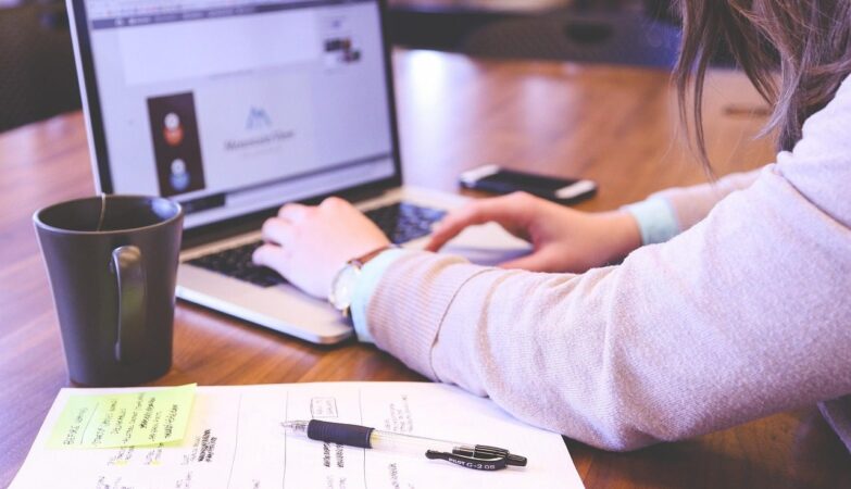 Business owner typing on a laptop beside notes and a coffee mug