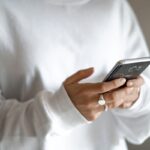 How households can swap impulse spending for a planned budget and repayments: a person in a white jumper checking their household budget on a mobile phone