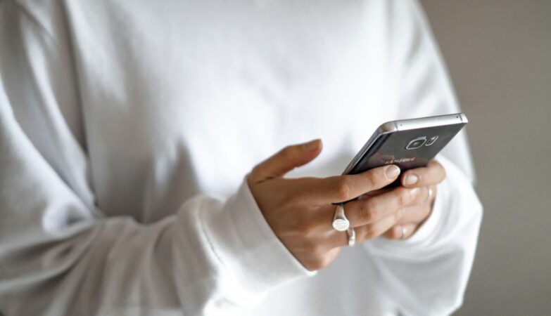 How households can swap impulse spending for a planned budget and repayments: a person in a white jumper checking their household budget on a mobile phone