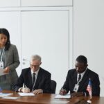 Business leaders sign an agreement at a conference table flanked by EU and US flags, illustrating practical Strategies Every Company Needs for International Business Disputes